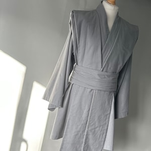 May include: A gray robe with a long, flowing design and a sash tied at the waist. The robe has a simple, elegant style.