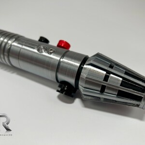 May include: A silver lightsaber with black and red accents. The lightsaber has a textured surface and a black and silver emitter.