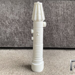 May include: A white plastic lightsaber prop with a detailed design. The lightsaber has a cylindrical body with a rounded top and a textured surface.