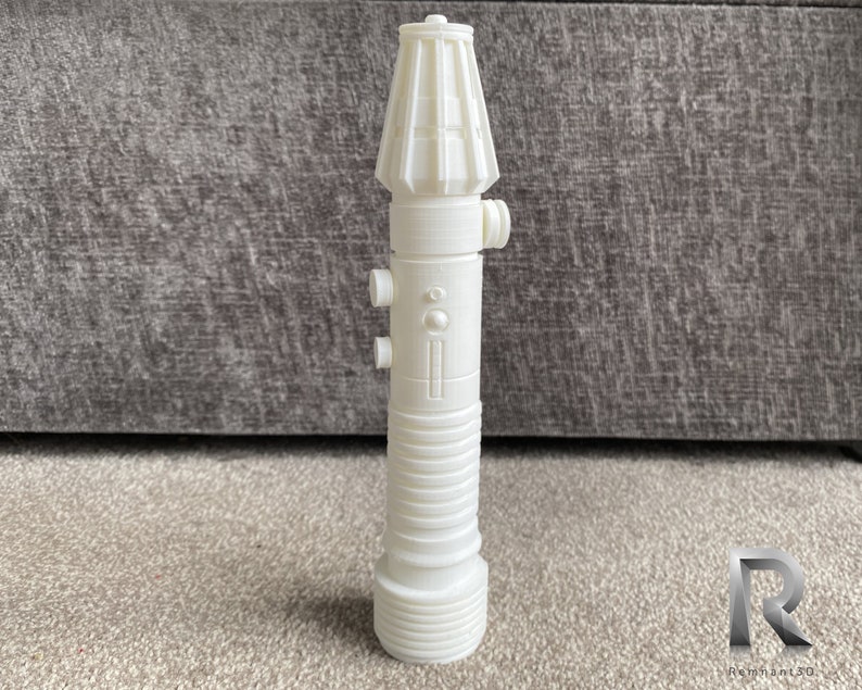 May include: A white plastic lightsaber prop with a detailed design. The lightsaber has a cylindrical body with a rounded top and a textured surface.