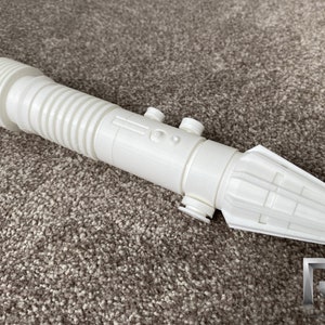 May include: White plastic lightsaber prop with a ribbed handle and a detailed hilt. The hilt has a small button and a textured design.