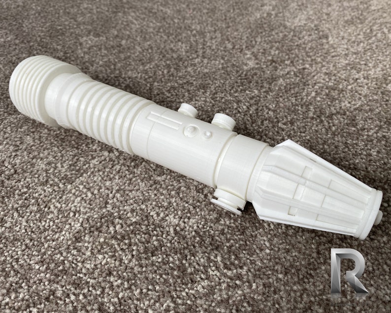 May include: White plastic lightsaber prop with a ribbed handle and a detailed hilt. The hilt has a small button and a textured design.