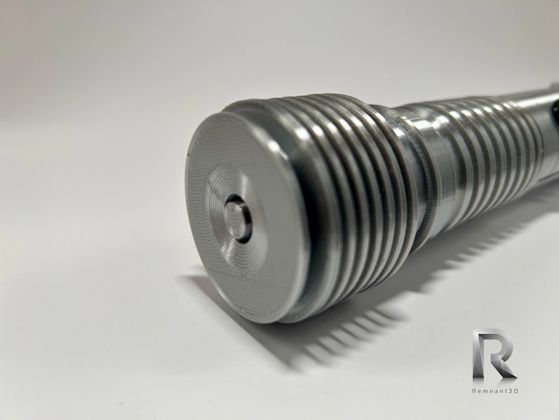 May include: Close-up of a silver metal lightsaber hilt with a textured, ribbed design. The hilt has a small, circular button on the end.