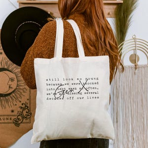 Pu&ograve; includere: Una borsa tote in tela color crema con testo stampato in nero che recita: still look so young because we were knocked into next week so often, Gen X we're all missing several decades off our lives. La borsa &egrave; dotata di due tracolle.