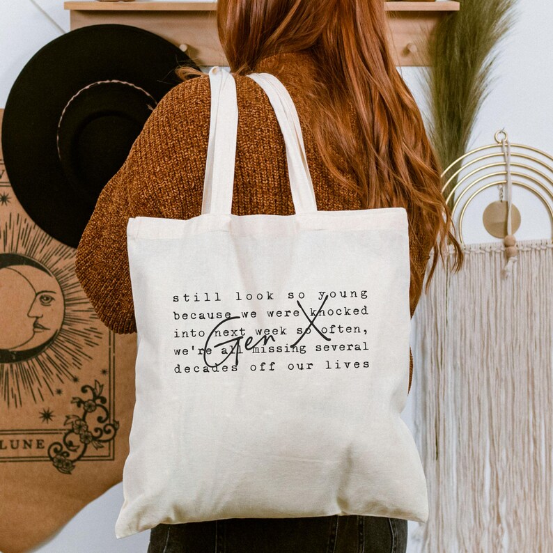 Pu&ograve; includere: Una borsa tote in tela color crema con testo stampato in nero che recita: still look so young because we were knocked into next week so often, Gen X we're all missing several decades off our lives. La borsa &egrave; dotata di due tracolle.