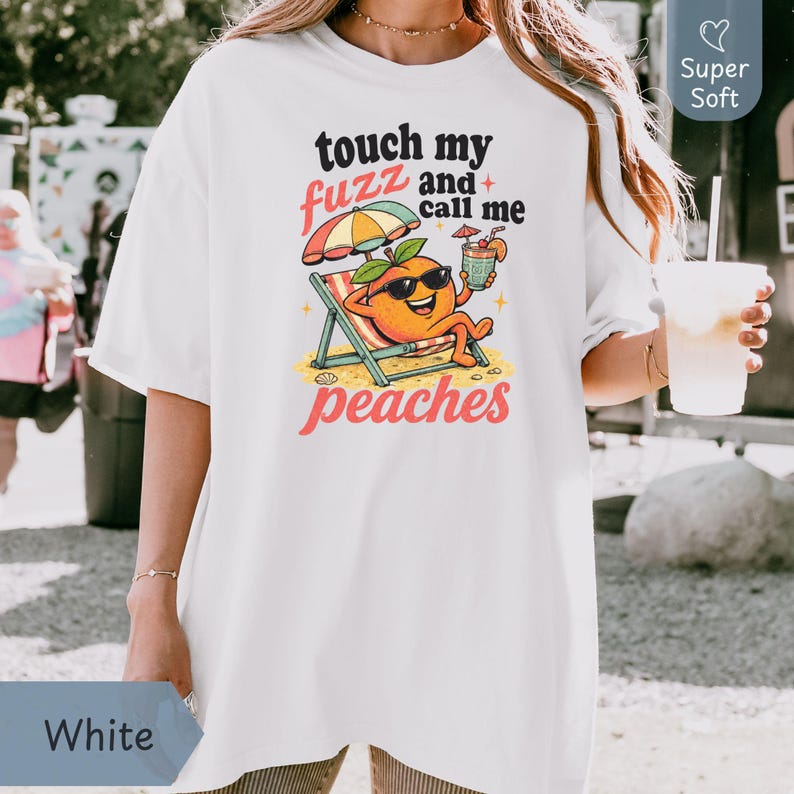 White oversized Comfort Colors shirt styled on a model, featuring a retro vintage cartoon peach with a cocktail reading 'touch my fuzz and call me peaches' for a chaotic girls trip vibe. Designed by experts at PhraseArtStudio - to solve the problem of stand-out matching bachelorette party wear.