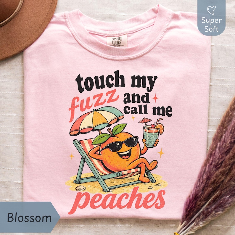 Blossom pastel pink-colored Comfort Colors shirt featuring a colorful retro cartoon peach sitting under a beach umbrella reading 'touch my fuzz and call me peaches' for a sassy summer vibe. Designed by experts at PhraseArtStudio - to solve the problem of finding a funny, zero-filter women's joke shirt.