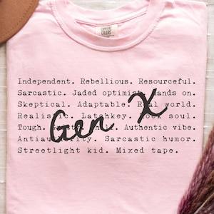 Blossom pink Comfort Colors Gen X humor t-shirt featuring sarcastic and satirical Gen X traits in a black typewriter-style font with handwritten “Gen X” overlay. Made from 100% ring-spun cotton, garment-dyed for a soft, vintage feel, and pre-shrunk for long-lasting comfort. Displayed flat with a tan hat and dried flowers for a warm, nostalgic aesthetic. Perfect for Generation X adults who appreciate humor, retro 80s 90s vibes, and authentic self-expression. Great funny Gen X gift