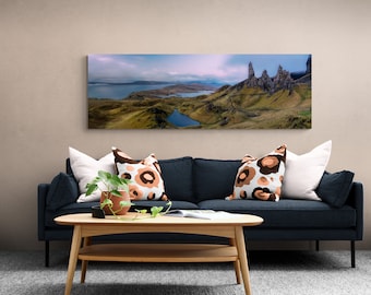 May include: A dark blue sofa with two white and brown patterned cushions and a white cushion. A potted plant sits on a wooden coffee table in front of the sofa. A panoramic landscape photograph of a rocky mountain range hangs on the wall above the sofa.