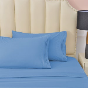 May include: Two light blue pillowcases on a light blue bed sheet with a white headboard. The bed is made and the pillowcases are smooth.