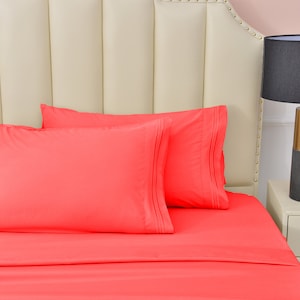 May include: A coral pink bed with two matching pillowcases and a white headboard. The bed is made with a smooth, wrinkle-free fabric.
