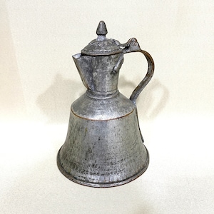 May include: A silver metal pitcher with a rounded, bell-shaped body and a handle. The pitcher has a decorative top with a pointed finial.