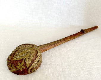 May include: A wooden ladle with a carved design. The ladle is decorated with gold-colored metal accents. The handle is long and slender.