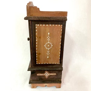 May include: A small wooden cabinet with a single door and intricate bone inlay designs. The cabinet has a dark brown finish and a light brown interior. The door has a small metal knob.