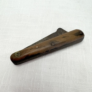 May include: A vintage pocket knife with a wooden handle and a metal blade. The handle is dark brown and has a slight patina. The blade is closed and has a slight curve.