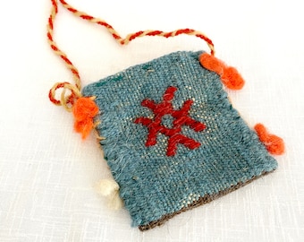 May include: A small blue woven bag with a red star design and orange and white tassels. The bag has a brown leather trim and a long tan cord.