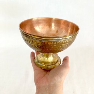 Könnte beinhalten: Eine kleine, gehämmerte Kupferschale mit einem goldfarbenen Sockel. Die Schale hat ein dekoratives, geätztes Design am Rand.