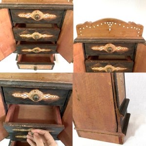 May include: A wooden jewelry box with four drawers, each with intricate inlaid designs. The box is painted black and has a light brown interior. The top drawer is open, revealing the empty space inside.