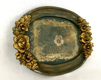 May include: A decorative oval tray with a dark green painted surface and gold painted floral accents. The tray has a raised edge and a slightly distressed look.