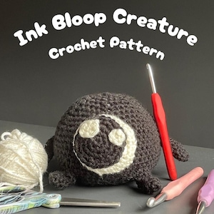 May include: A crocheted black Ink Bloop Creature with a white face design. The image includes crochet hooks, scissors, and a ball of white yarn. Text at the top reads "Ink Bloop Creature Crochet Pattern."