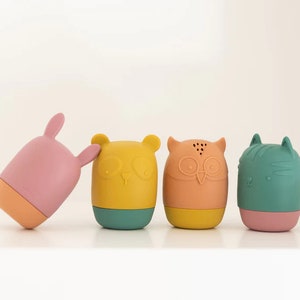K&ouml;nnte beinhalten: Vier bunte Silikon-Badetiere in Tierform: ein rosa Kaninchen, ein gelber B&auml;r, eine orange Eule und eine gr&uuml;ne Katze. Jedes Spielzeug hat einen anderen Gesichtsausdruck und Merkmale.