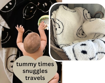 Könnte beinhalten: Schwarz-cremefarbene Babydecke mit einem sich wiederholenden Smiley-Gesicht-Muster. Die Decke ist weich und flauschig, geeignet für Bauchzeit, Kuscheln, Reisen und Nickerchen. Der Text auf dem Bild lautet: tummy times, snuggles, travels, naps.