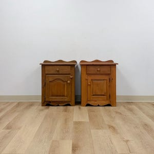 May include: Two matching wooden nightstands featuring a medium brown finish, each constructed with a single top drawer and a lower cabinet door. Both units include a scalloped edge along the top and bottom, with small round wooden knobs on the drawer and door.