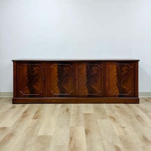 May include: A long, low-profile wooden sideboard featuring four cabinet doors. Each door displays a rich, dark brown wood grain pattern with a distinct flame-like veneer design and a subtle, raised rectangular border frame around the center panel.