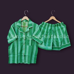 Può includere: Pigiama a righe verdi e bianche con una camicia a maniche corte abbottonata e pantaloncini. La camicia ha una tasca sul lato sinistro. I pantaloncini hanno una cintura elastica. Il set è appeso a grucce di legno. @uniquecraftsfabric