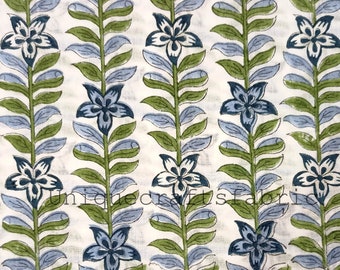May include: White fabric with a repeating pattern of blue and green floral designs. The flowers are stylized and have five petals. The stems are thin and have small leaves.