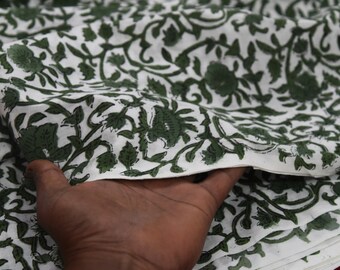 May include: White cotton fabric with a green floral print. The fabric is folded and a hand is holding the top layer.