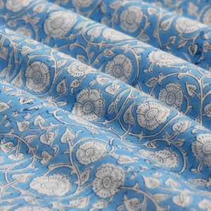 May include: Blue fabric with a white floral pattern. The fabric has a repeating pattern of white flowers and leaves on a light blue background.