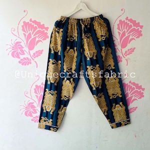 以下が含まれることがあります： 黄色の虎が繰り返しプリントされたストライプ柄のターコイズブルーのパジャマパンツ。パンツはドローストリングウエストです。