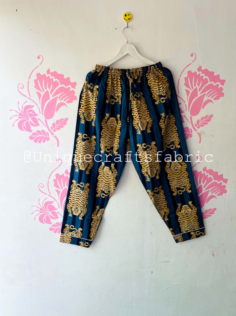 以下が含まれることがあります： 黄色の虎が繰り返しプリントされたストライプ柄のターコイズブルーのパジャマパンツ。パンツはドローストリングウエストです。