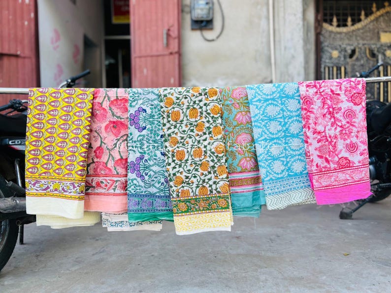 Pu&ograve; includere: Sei pannelli di tessuto con motivi diversi sono appesi a una barra di metallo. I pannelli sono di vari colori, tra cui giallo, rosa, verde, blu e bianco. I pannelli sono tutti in cotone e hanno una variet&agrave; di motivi floreali e geometrici.