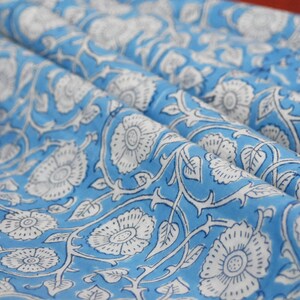 May include: A blue fabric with a white floral pattern. The fabric has a repeating pattern of white flowers with a blue center on a light blue background.