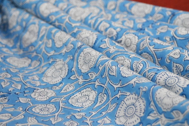May include: A blue fabric with a white floral pattern. The fabric has a repeating pattern of white flowers with a blue center on a light blue background.