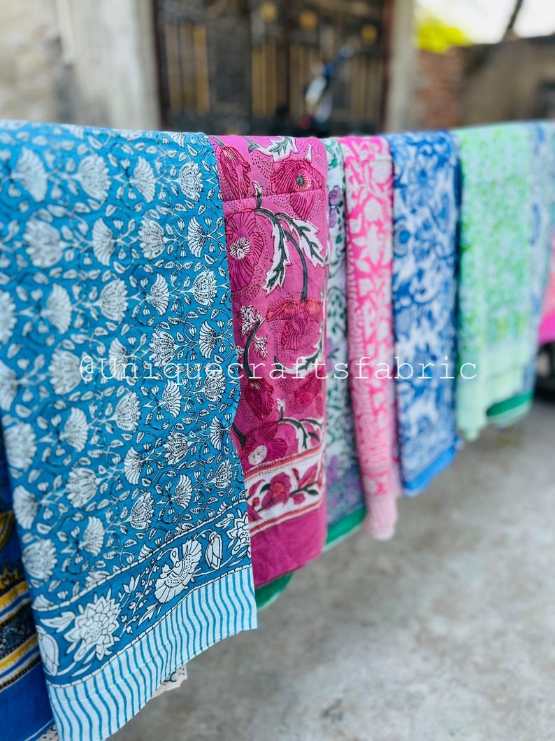 Pu&ograve; includere: Una collezione di sei sciarpe di cotone stampate a colori vivaci con motivi floreali. Le sciarpe sono appese a uno stendino.