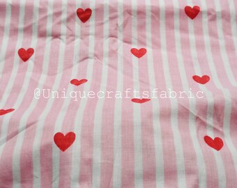 May include: Pink and white striped fabric with a pattern of red hearts. The fabric has vertical stripes and the hearts are evenly spaced across the material. The text "@Uniquecraftsfabric" is visible on the fabric.