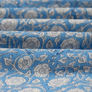 May include: Blue fabric with a white floral pattern. The fabric is folded in several layers, showing the pattern repeating.
