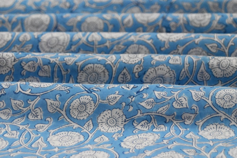 May include: Blue fabric with a white floral pattern. The fabric is folded in several layers, showing the pattern repeating.