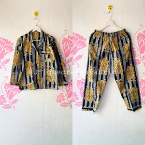 以下が含まれることがあります： 金色の虎柄のグレーとブラックのストライプのパジャマセット。セットには、ボタンダウンカラーの長袖シャツとそれに合わせたパンツが含まれています。