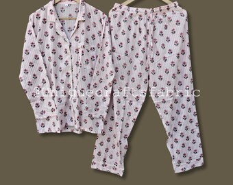 May include: A two-piece pajama set with a floral pattern. The set includes a button-down shirt and matching pants. The pajamas are light pink with vertical stripes and small, dark pink floral designs. The shirt has a collar and a chest pocket.