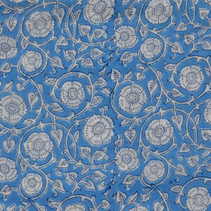 May include: A blue fabric with a white floral pattern. The pattern features small white flowers with a center circle and a ring of petals, surrounded by leaves and vines.
