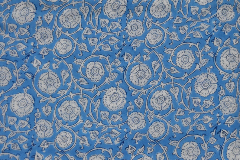 May include: A blue fabric with a white floral pattern. The pattern features small white flowers with a center circle and a ring of petals, surrounded by leaves and vines.