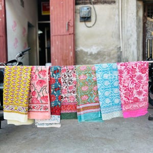 Pu&ograve; includere: Una collezione di sei sciarpe di stoffa colorate con motivi floreali. Le sciarpe sono appese a un filo da bucato e sono disposte in fila. Le sciarpe sono fatte di cotone e sono morbide e comode da indossare.