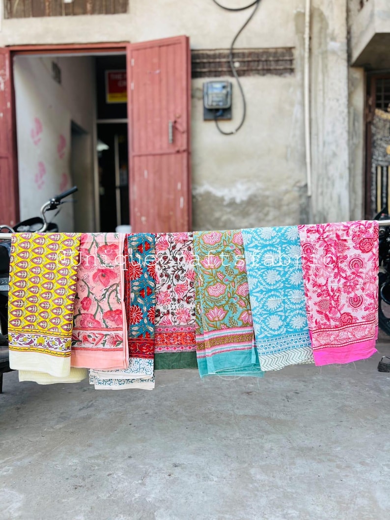 Pu&ograve; includere: Una collezione di sei sciarpe di stoffa colorate con motivi floreali. Le sciarpe sono appese a un filo da bucato e sono disposte in fila. Le sciarpe sono fatte di cotone e sono morbide e comode da indossare.