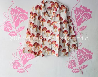Puede incluir: Camisa blanca de manga larga con estampado de setas rojas y blancas. La camisa tiene un cierre de botones en la parte delantera y un bolsillo en el lado izquierdo.