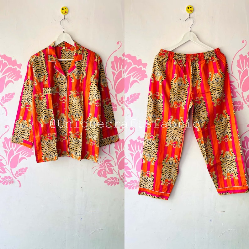 以下が含まれることがあります： ピンクとオレンジのストライプ柄に虎柄がプリントされたパジャマセット。トップスは襟付きで長袖。パンツは長ズボンで、ウエストは紐で調節できます。