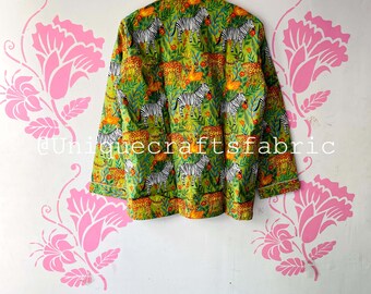 May include: A green button-up shirt with a white trim and a zebra and leopard print. The shirt is hanging on a hanger against a white wall with pink floral stencils.
